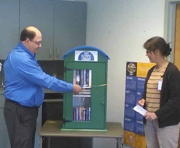 Mayor Monohon cuts the tiny ribbon on the new tiny library that will reside at the Forks Transit Center as Forks Librarian Teresa Tetreau looks on.