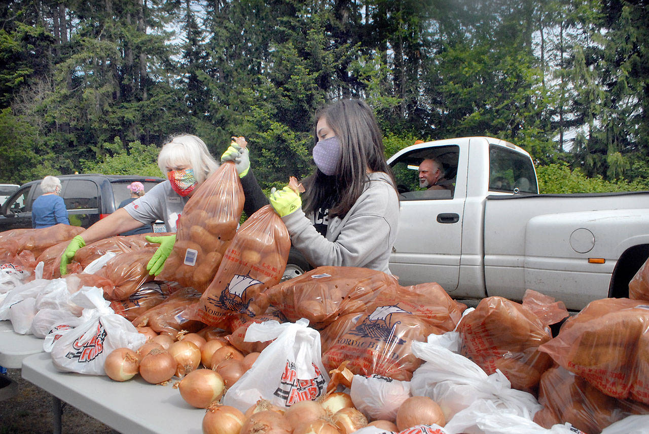 Volunteers Delores Hampton, left, and Tavita Bucio, both of Sequim, pick up bags of potatoes and onions for placement into a waiting vehicle during a giveaway Saturday, May 23, 2020, in the parking lot at the Clallam County Fairgrounds in Port Angeles. Dozens of volunteers distributed a portion of about 50,000 pounds of potatoes and 3 tons of onions during the event, which included a similar giveaway in Forks. (Keith Thorpe/Peninsula Daily News)