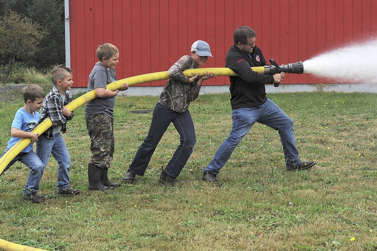 Pastor/chaplain Andy Pursley helps a group of grade school students handle the hose Friday, Sept 18 at the Beaver Fire Hall where these youngsters besides taking a ride on the fire truck learned the ways of fire fighting. Local fire departments are always searching for volunteer firemen. Perhaps Fire District #1 Beaver has found some future recruits. Photos by Lonnie Archibald