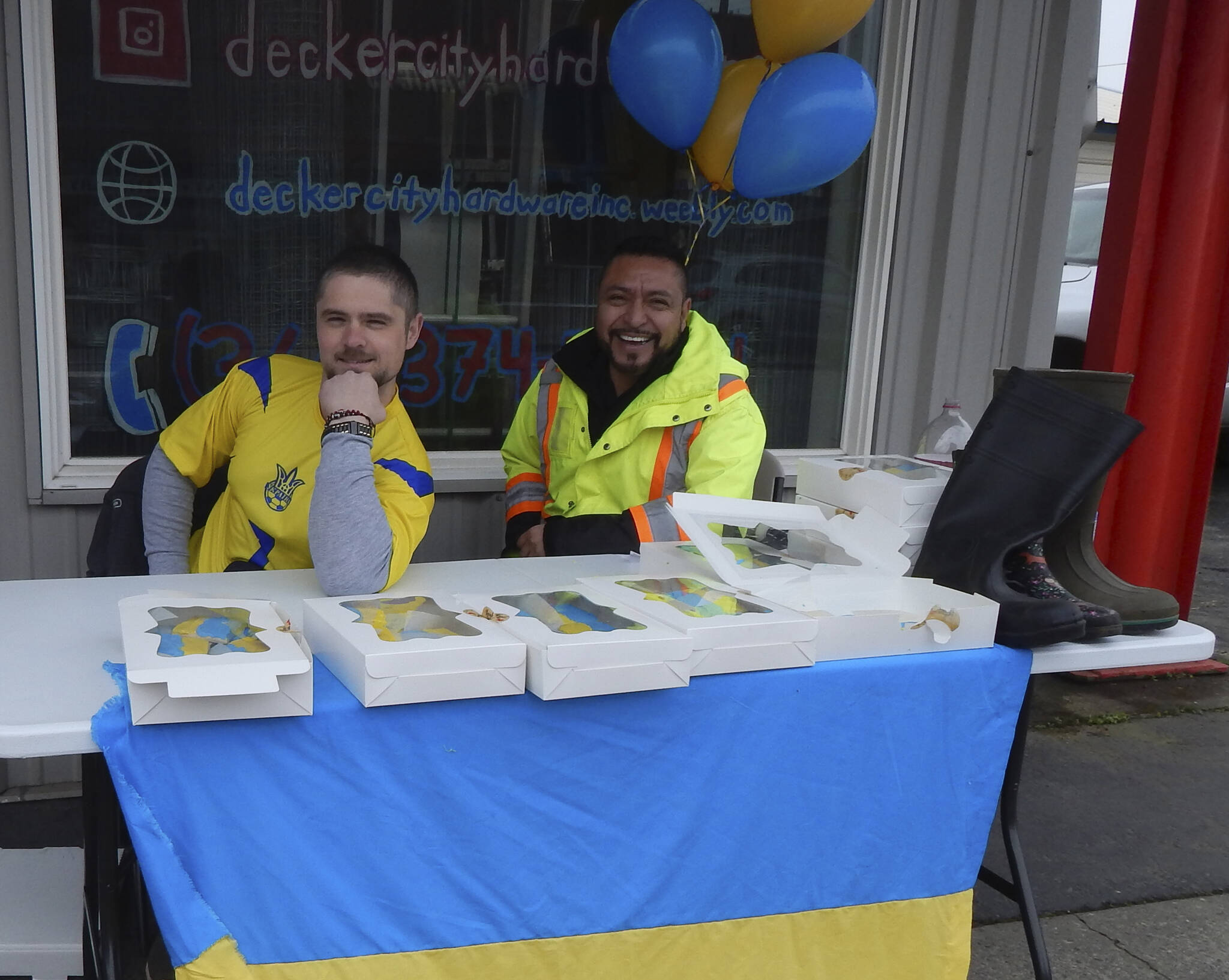 Sergei Holmquist on the left, in the photo, was joined by Juan Almazan for support. Empty boots on the table await donations for Ukraine on Friday afternoon outside Decker City Hardware. Photo Christi Baron