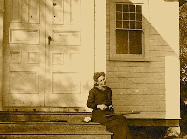 Mina sitting on the steps of the Quillayute Prairie Church, her gun beside her on the step.