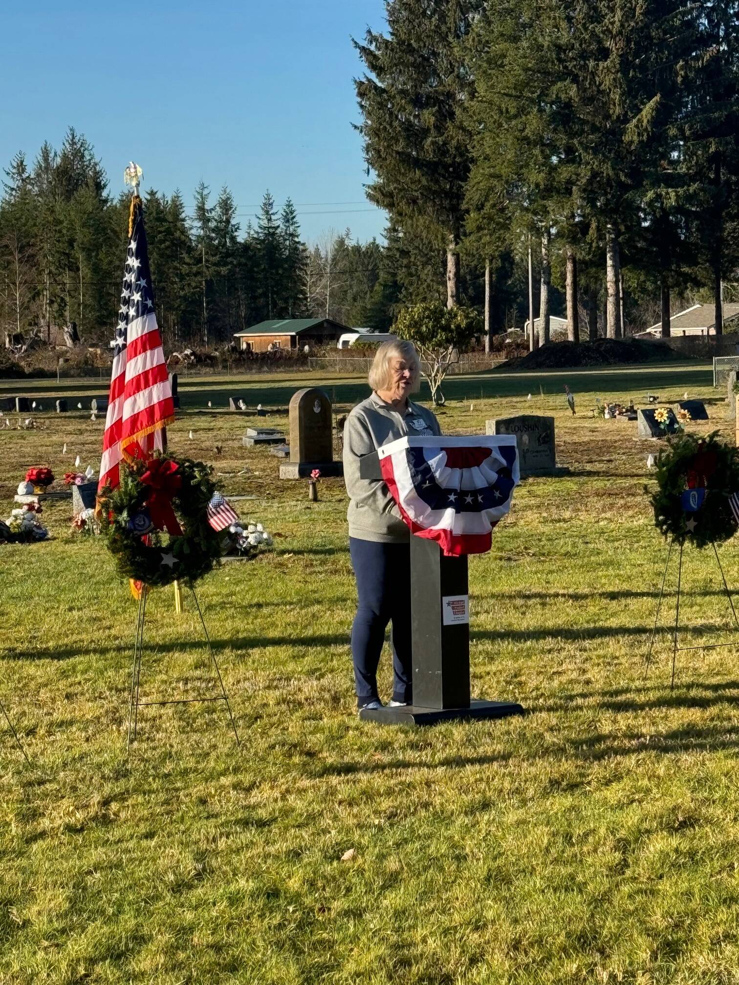 Local member of the Michael Trebert Chapter of DAR, Ilene Rogers, speaks at the Forks Cemetery on December 16 during the Wreaths Across America Ceremony. Also offering a message during the ceremony was Pastor Bob Schwartz of the Forks First Baptist Church. Across the US 3,700 locations participated in the ceremonies.