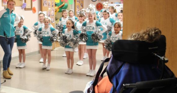 In honor of May Day members of the Coastal Cheer Academy made a visit to Forks Community Hospital Wednesday afternoon and treated the residents at LTC to some cheers and some flowers!
There are about two dozen members in CCA and they are ages seven to 13. They performed several cheers and stunts in their new uniforms and then distributed flowers to everyone. One of the coaches, Melanie Stonebreaker, seen at the left in the photo, shared that the community has given so much in getting them started that they wanted to give something back. Here a LTC resident looks on as the group gets ready to give an enthusiastic cheer! Photo Christi Baron