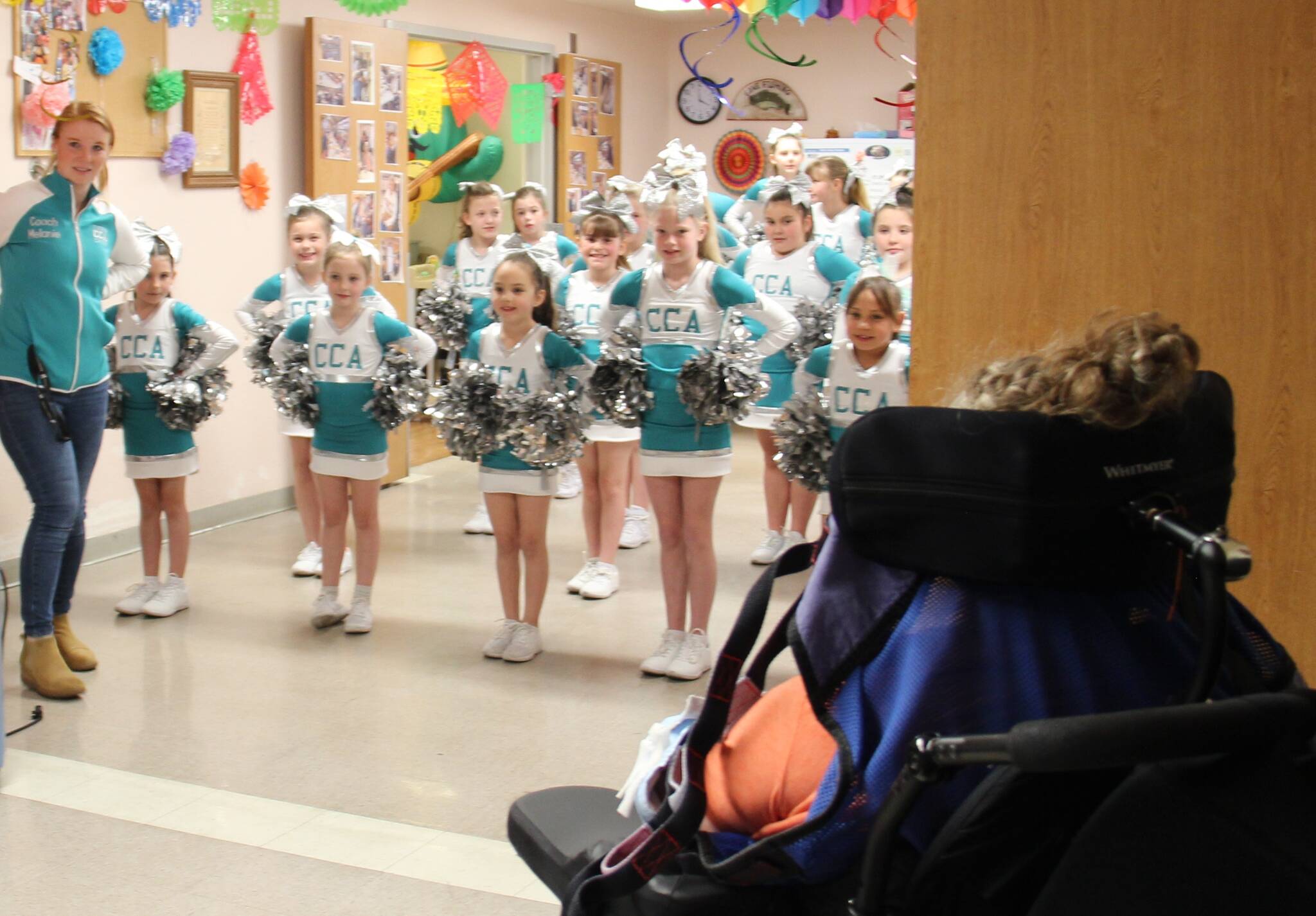 In honor of May Day members of the Coastal Cheer Academy made a visit to Forks Community Hospital Wednesday afternoon and treated the residents at LTC to some cheers and some flowers!
There are about two dozen members in CCA and they are ages seven to 13. They performed several cheers and stunts in their new uniforms and then distributed flowers to everyone. One of the coaches, Melanie Stonebreaker, seen at the left in the photo, shared that the community has given so much in getting them started that they wanted to give something back. Here a LTC resident looks on as the group gets ready to give an enthusiastic cheer! Photo Christi Baron