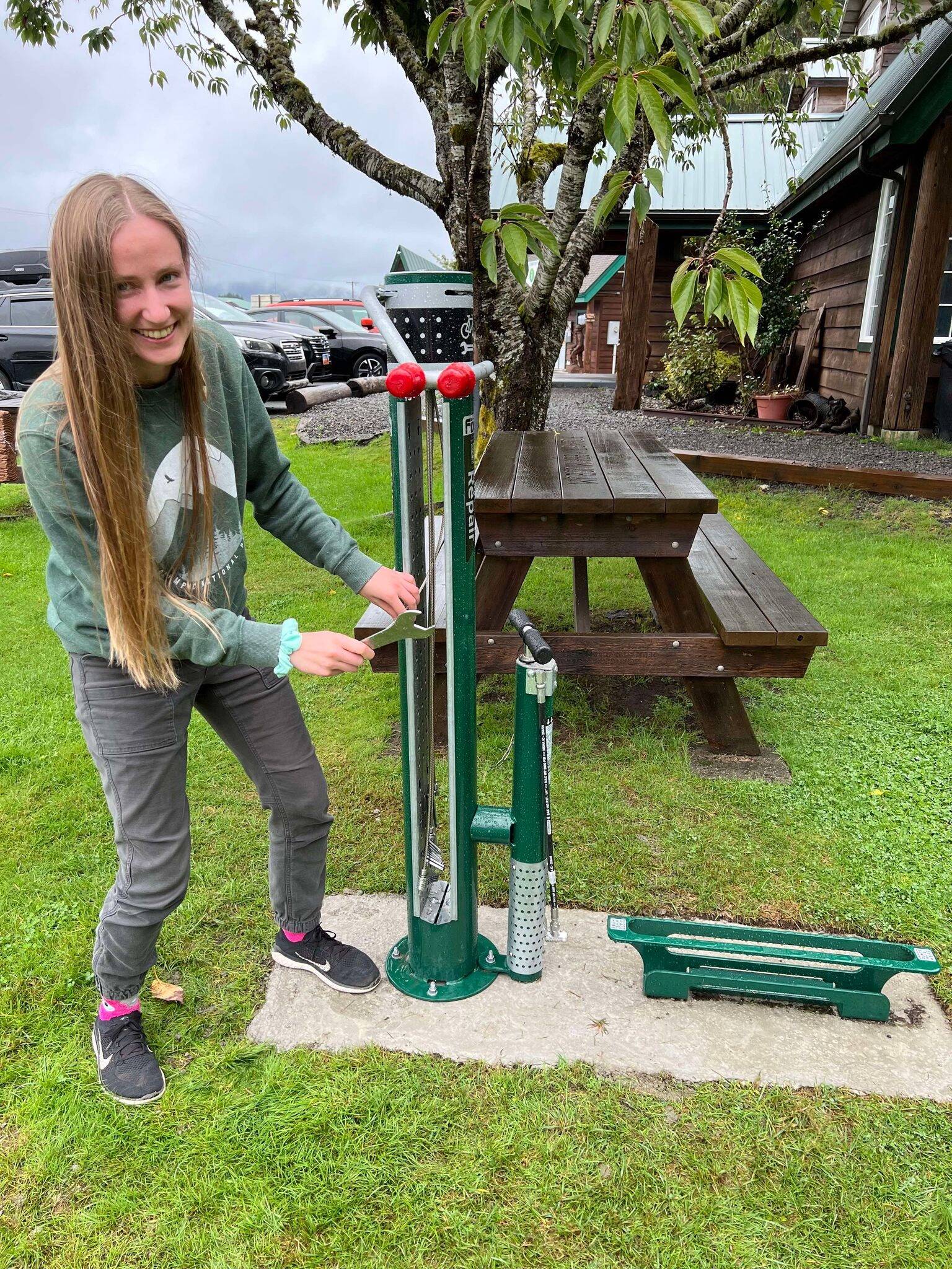 Provided through a grant from the Olympic Peninsula Visitor Bureau, the Forks Chamber purchased a bike rack and repair station for the VIC/Timber Museum grounds. These pieces were added so that bicyclists traveling through could rest and repair their bikes at a safe location. With the help of Olympic Corrections Center Community Crews, they were installed over the last two weeks.
Pictured: Kari Larson, Forks Chamber Director of Customer Service, inspects the new additions! Submitted photo